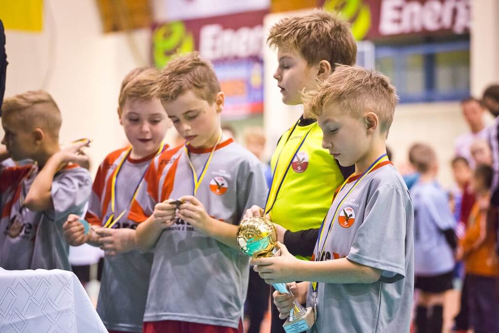 Młodzi piłkarze z klubu OTS Korona Ostrołęka cieszą się ze zwycięstwa w turnieju. Ich radość pokazuje dumę z osiągnięcia celu i pracy zespołu. Firma KDF-Podatki wspiera rozwój tych utalentowanych sportowców.